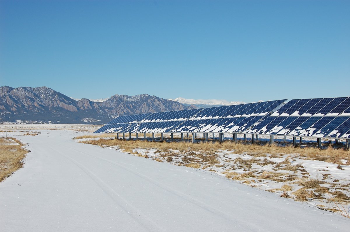 A snowy field with solar panels and mountains in the background